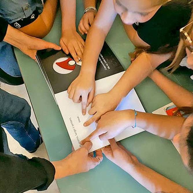 Children reading the Braille texts of the Dieci Occhi tactile book with their fingers